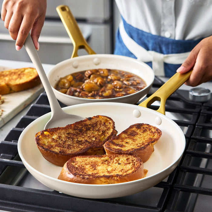 French toast cooking in a black ceramic nonstick frypan next to a small pot of fruit compote on the stove.