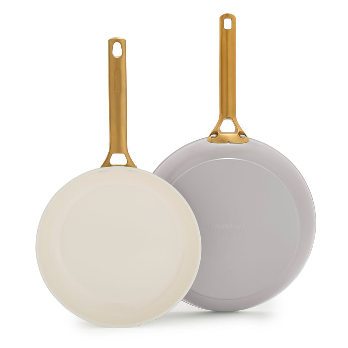Two taupe gray frying pans with gold handles on a white background