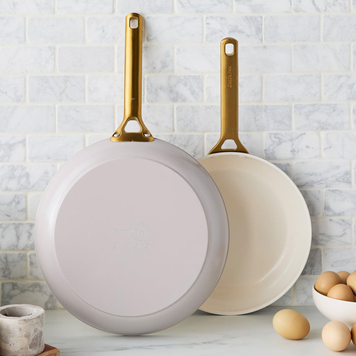 Two taupe gray frying pans with gold handles on a kitchen counter with eggs and a bowl.