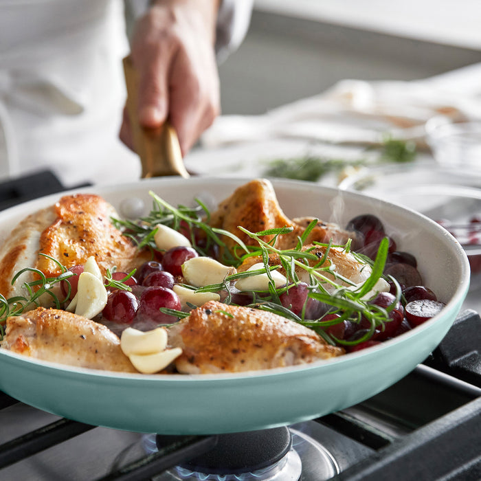 Light blue frying pan with roasted chicken, grapes, and herbs on a stove