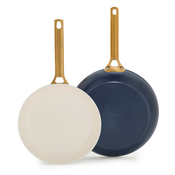 Two dark blue frying pans with gold handles on a white background