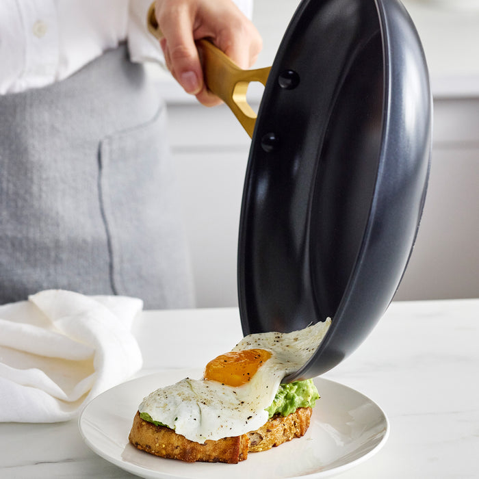 Person pouring an egg from a black frying pan onto toast on a white plate.