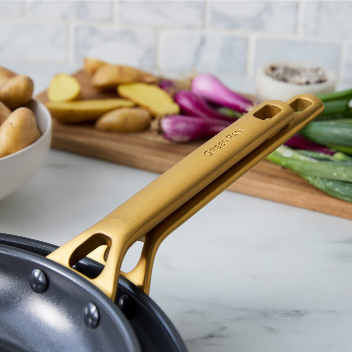 Gold-handled black frying pan on a kitchen counter with vegetables in the background