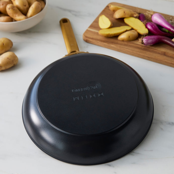 Black frying pan on a marble surface with potatoes and onions in the background