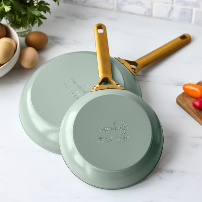 Two green frying pans with gold handles on a white surface.
