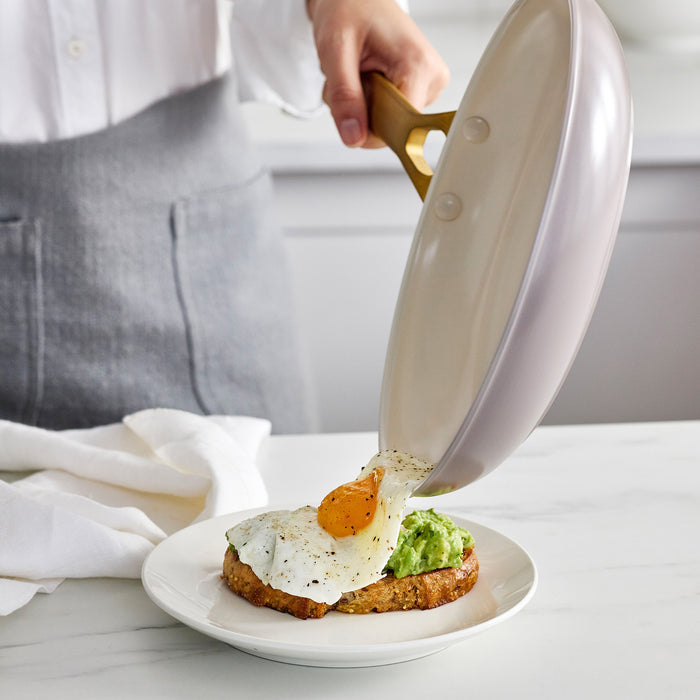 Person pouring a dish from a taupe gray pan onto a plate with avocado and egg.