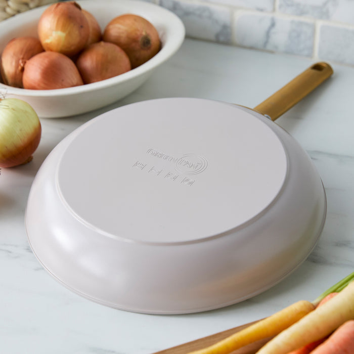 Taupe gray frying pan with a gold handle on a kitchen counter with onions and carrots.