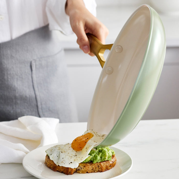 Person using a green frying pan to place an egg on a piece of avocado toast