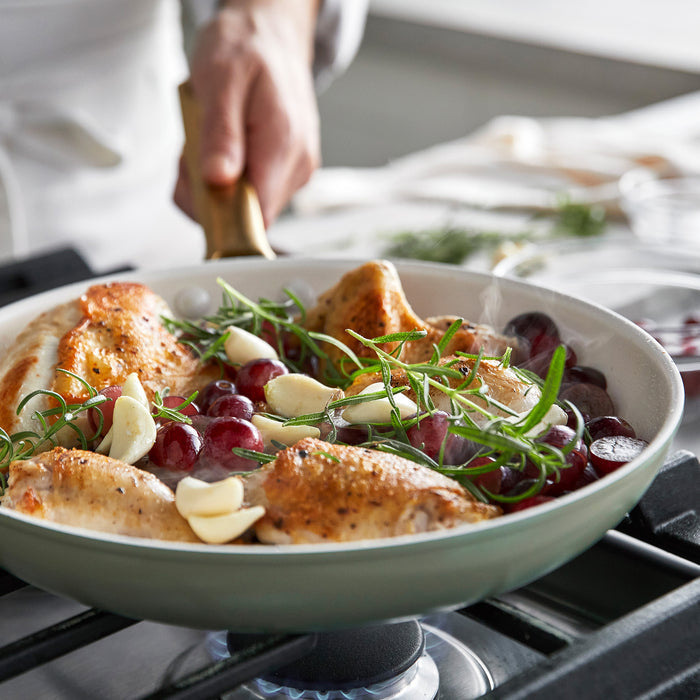 Frypan with roasted chicken dish with grapes and herbs on a stove