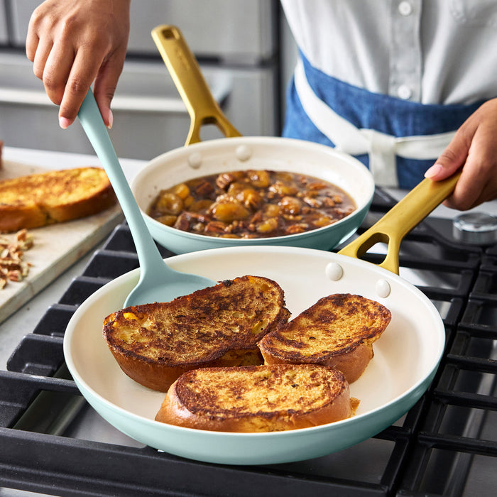 Person serving French toast from a light blue frying pan on a stove.