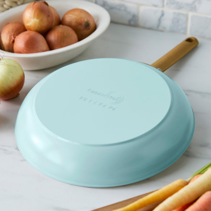 Light blue frying pan on a kitchen counter with onions and carrots.