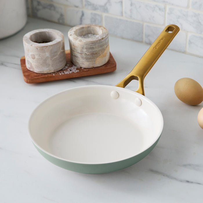 Green frying pan with gold handle on a kitchen counter