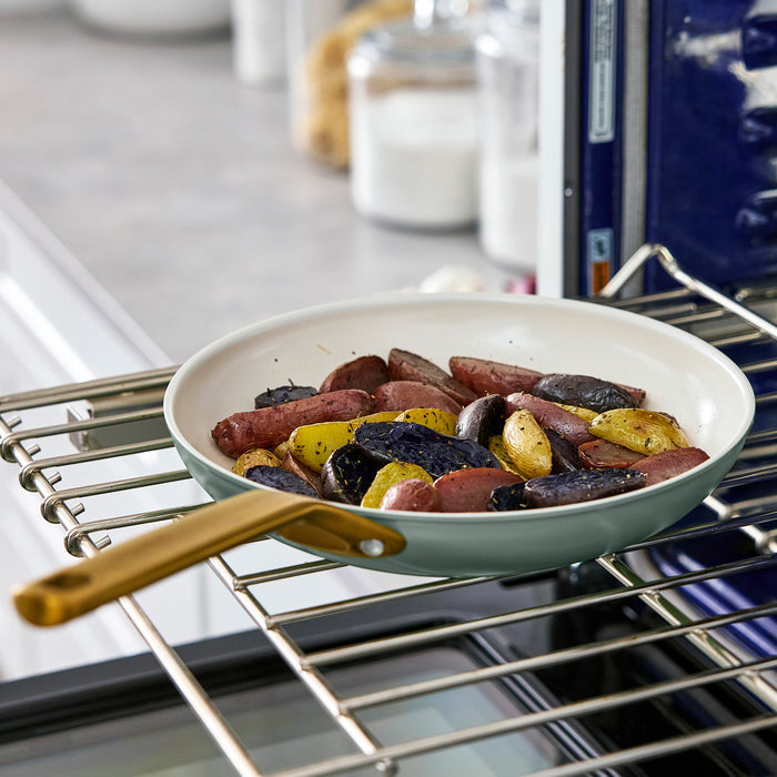 Green pan with sausages and potatoes in an oven