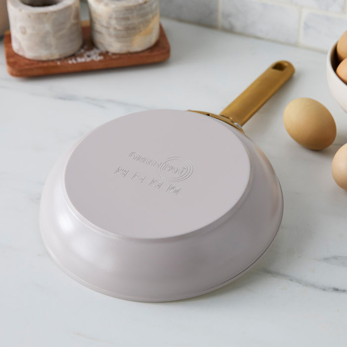 Taupe gray frying pan with a gold handle on a marble countertop.