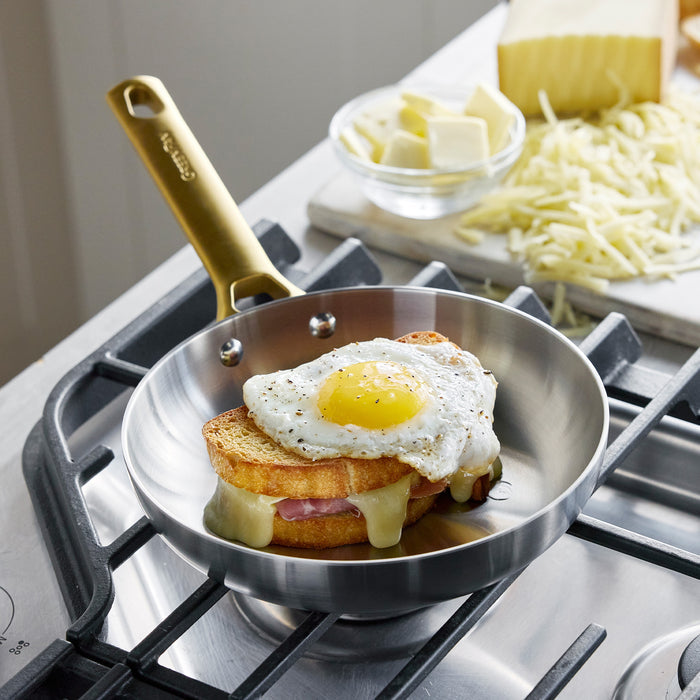 Fried egg on toast in a frying pan on a stove with cheese and butter in the background.