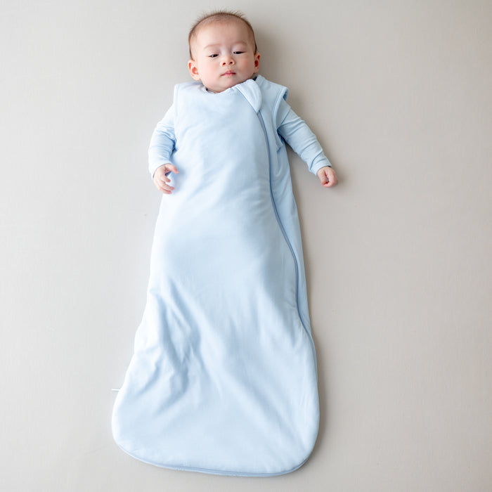 Baby wrapped in a light blue sleep bag on a neutral background