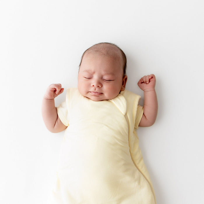 Newborn baby wearing in a yellow sleep bag on a white background