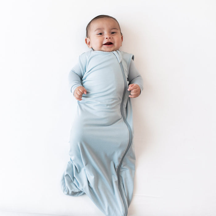 Baby modeling the 0.5 Tog Sleep Bag in Fog with a Fog long sleeve romper underneath