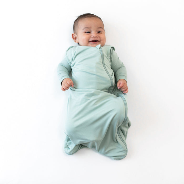 Smiling infant wearing the  0.5 Tog Sleep Bag in Sage with a Sage long sleeve romper underneath