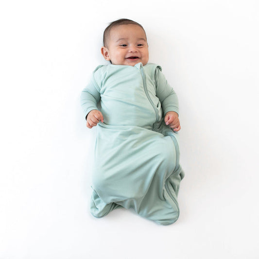 Smiling infant wearing the  0.5 Tog Sleep Bag in Sage with a Sage long sleeve romper underneath