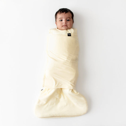 Baby wrapped in a pale yellow-colored swaddle on a white background