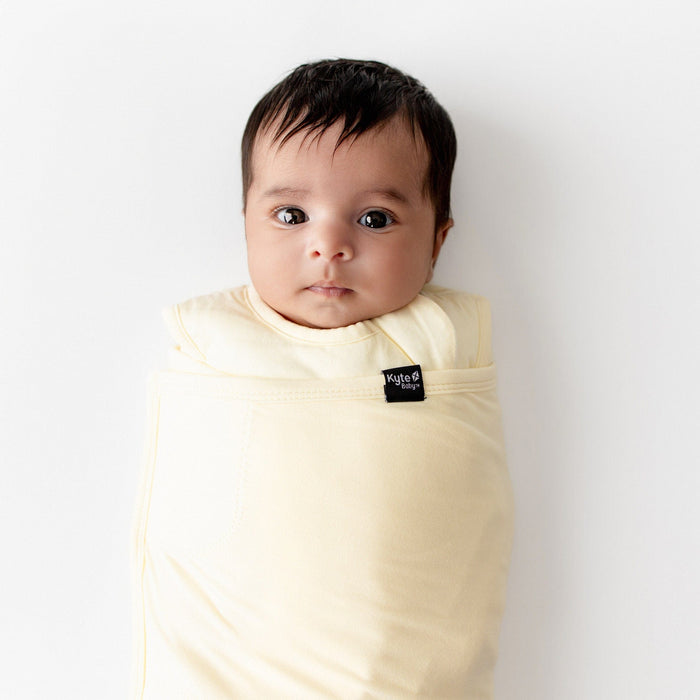 Baby wrapped in a yellow colored swaddle with a visible kyte baby label on a white background