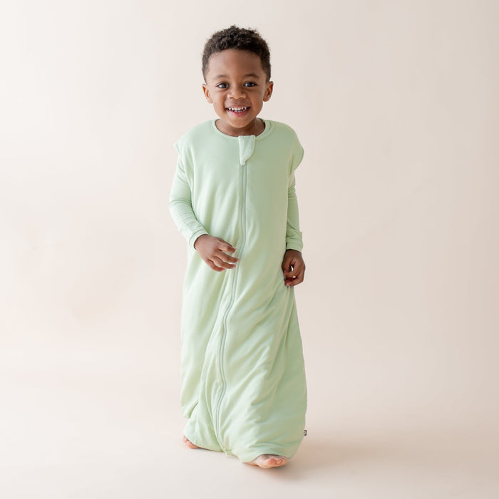Child wearing a light green sleep bag walker against a plain background