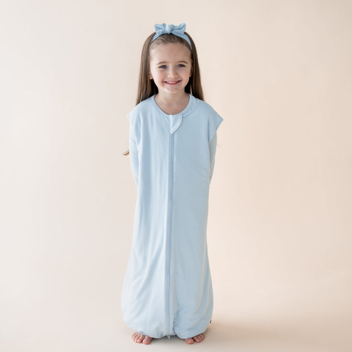 Young girl wearing a light blue sleeveless sleep bag walker with a zipper on a beige background