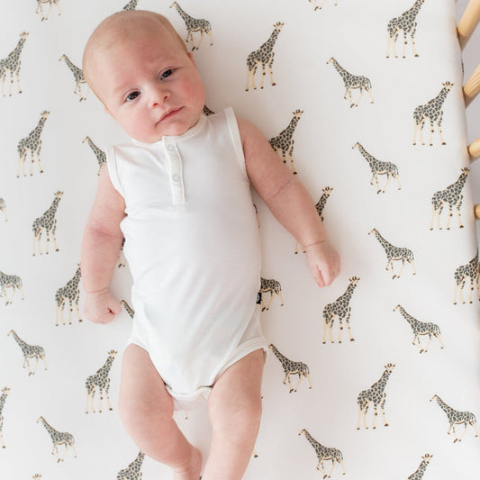 Infant laying on a crib sheet in Giraffe and wearing Kyte Baby Sleeveless  Bodysuit in Cloud