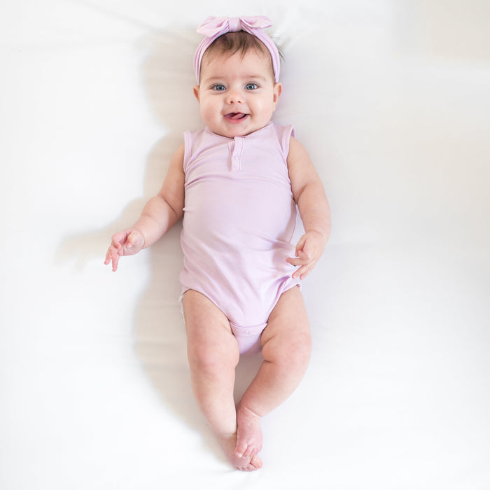 Baby wearing a sleeveless bodysuit and bow in a light purple color