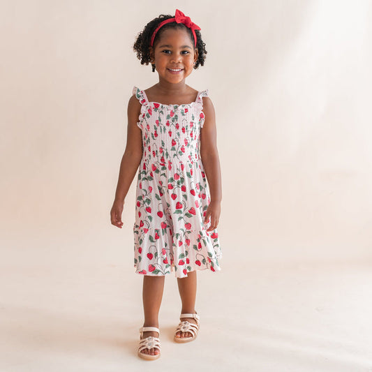 Young girl walking in front of a light beige background wearing the Smocked Dress in Strawberry Fields