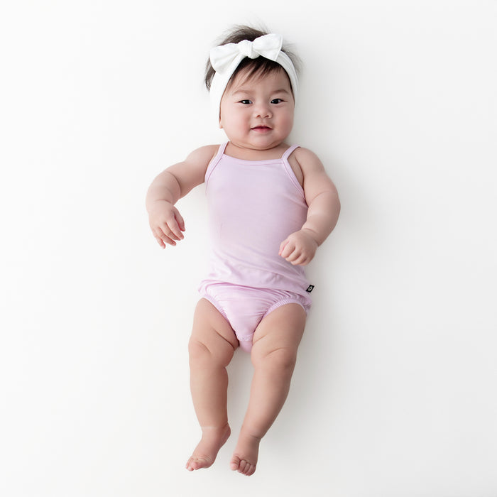 Infant girl wearing the Spaghetti Strap Leotard in Thistle with a white knotted bow laying on a white surface