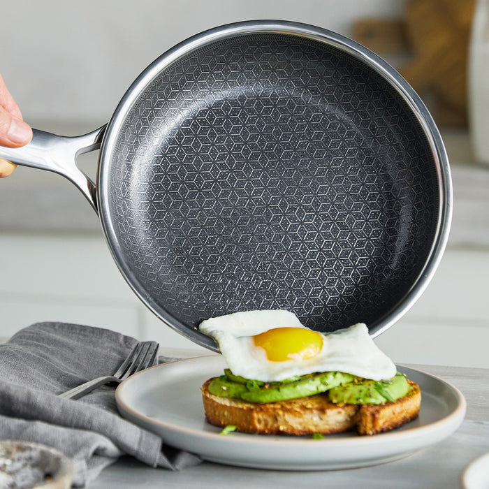 Hand uses a grey ceramic nonstick frypan to serve a fried egg onto avocado toast.
