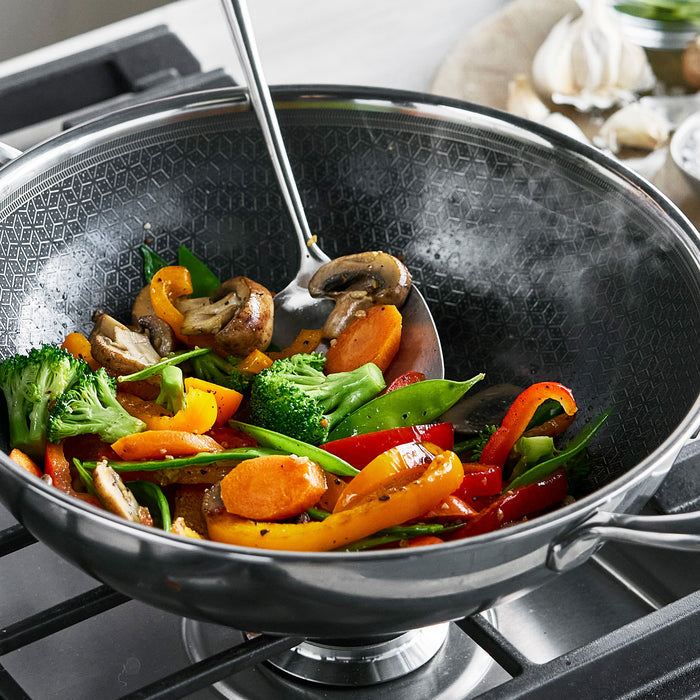 Stir-fry vegetables cooking in a gray ceramic nonstick 12-inch wok with glass lid.