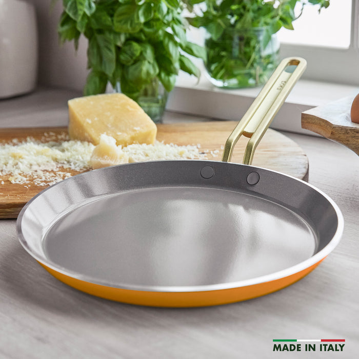 Yellow crepe pan on a kitchen counter with cheese and herbs.