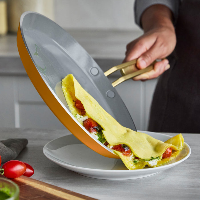 Person sliding a crepe from a pan onto a white plate