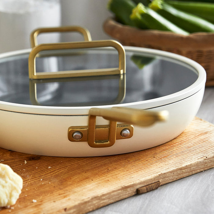 White ceramic 12-inch frypan with gold handle on a board next to chopped vegetables.