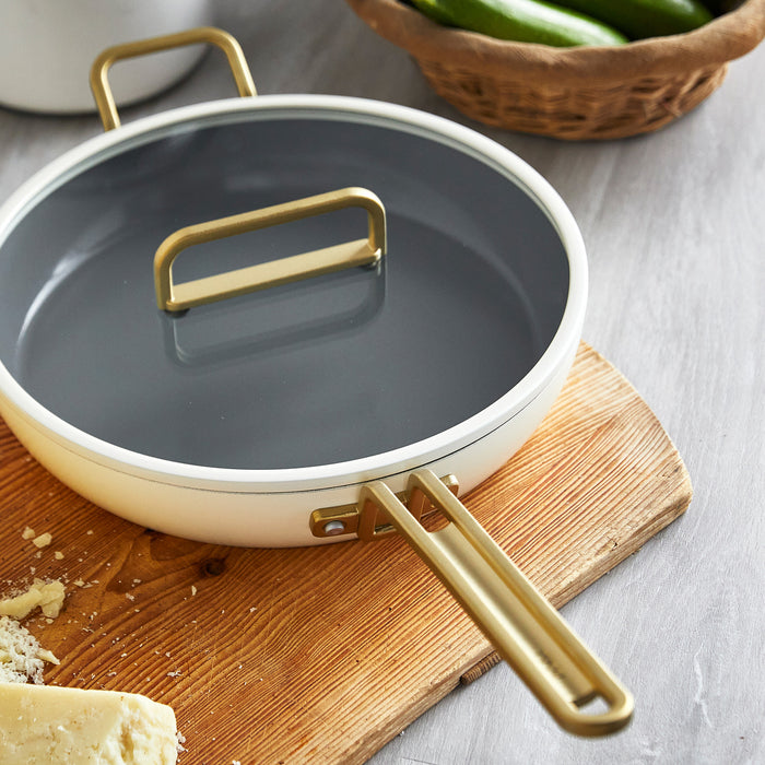 White ceramic 12-inch frypan with lid, resting on a board next to a wedge of cheese.