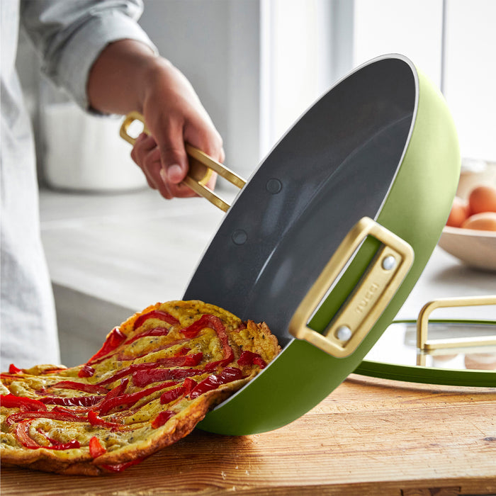 Vegetable frittata being slid from a ceramic nonstick frypan onto a wooden cutting board.