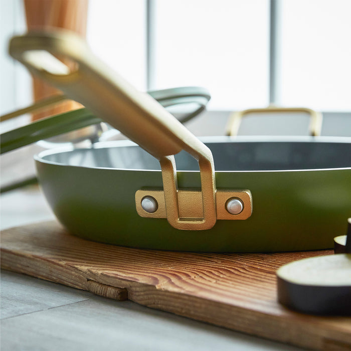 Stanley Tucci ceramic 12 frypan in green with gold handle, matching lid, and utensils visible in the background.