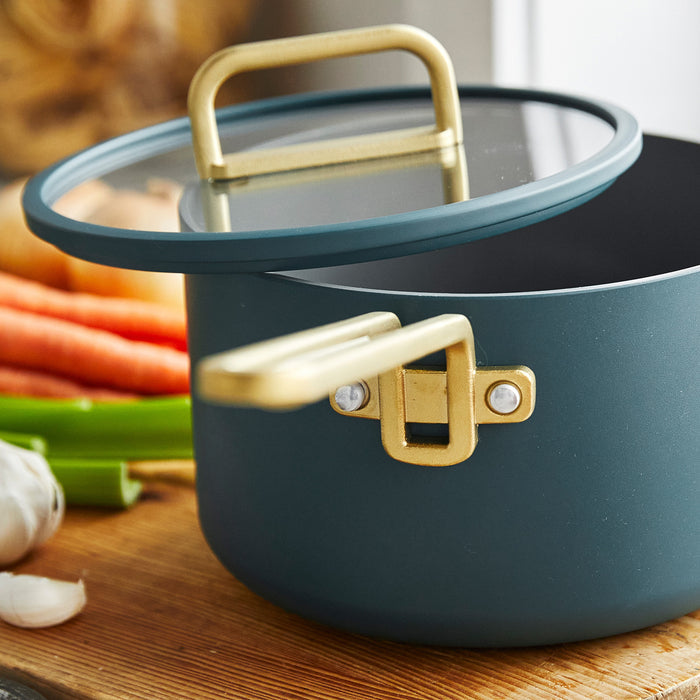 Venetian teal 4-quart saucepan with lid on a board, next to carrots, celery, and garlic.