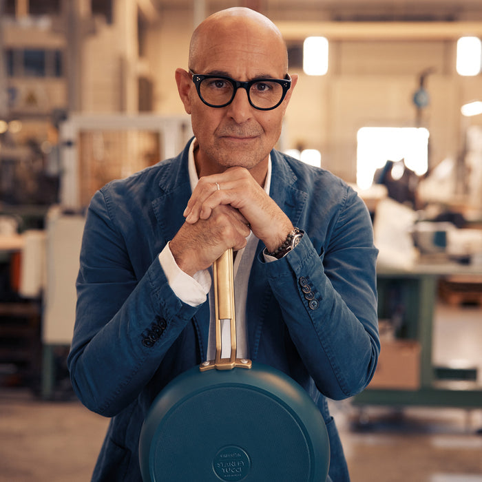 Stanley Tucci holding a teal frypan in an industrial setting