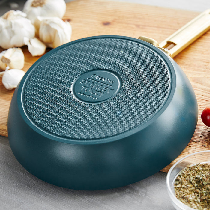 Venetian teal ceramic 8-inch frypan upside down on a wooden board, with garlic bulbs and fresh herbs nearby.