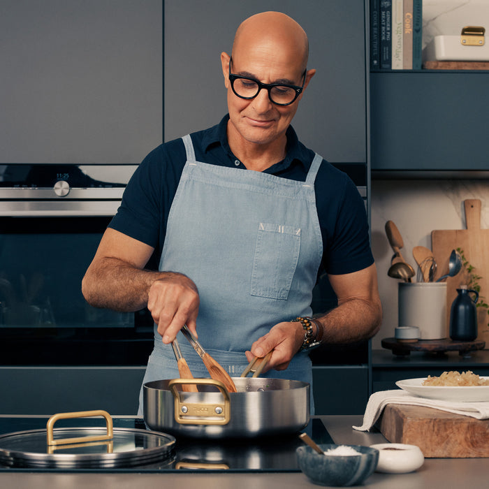 Man cooking with Stanley Tucci™ 11-piece cookware set and wooden utensils in a modern kitchen.