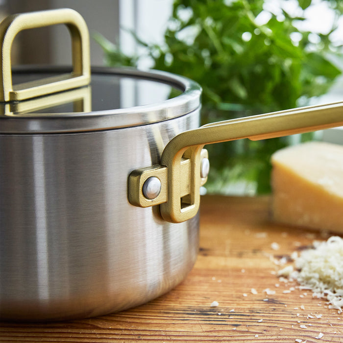 Stainless steel saucepan with ceramic nonstick finish and champagne handles on a wooden counter, 2-quart size.
