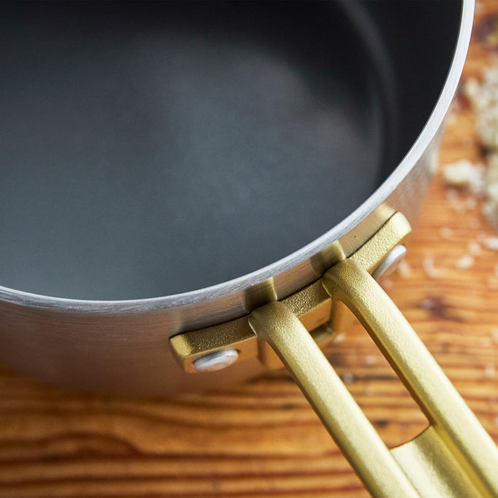 Stainless steel saucepan with a champagne-colored handle on a wooden surface, 2-quart size.