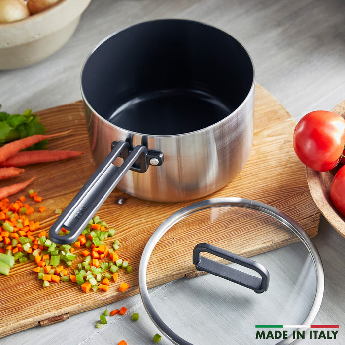 Stainless steel 4-quart saucepan with lid on a board next to chopped vegetables, tag reads Made in Italy.