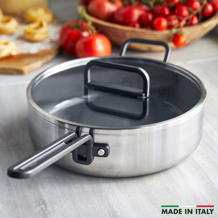 Stainless steel sauté pan with ceramic nonstick interior and glass lid on a kitchen counter.