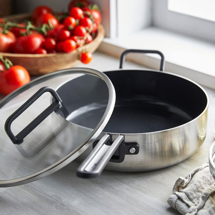 Stainless steel ceramic sauté pan with lid on a counter next to fresh tomatoes, 4-quart size.