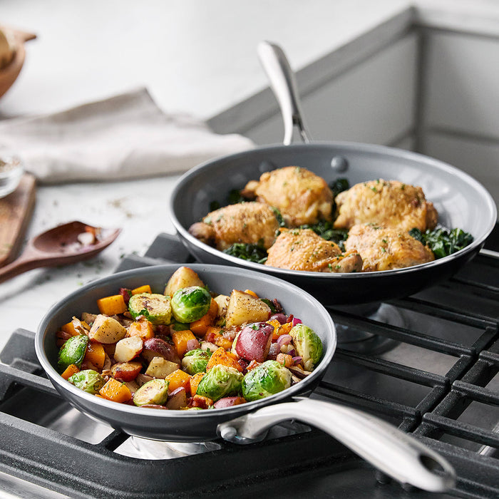 Set of two ceramic nonstick pans, one with chicken, greens and egg, the other with mixed roasted vegetables.